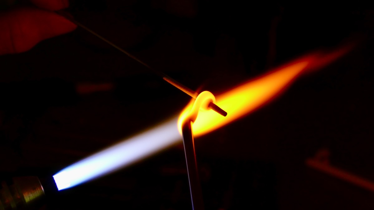Schmelzender Glasstab in oranger Flamme während der Perlenherstellung