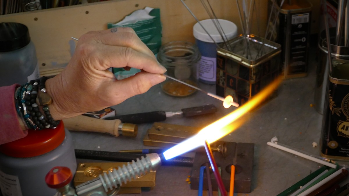 Eine Hand hält einen Glasstab über die Flamme