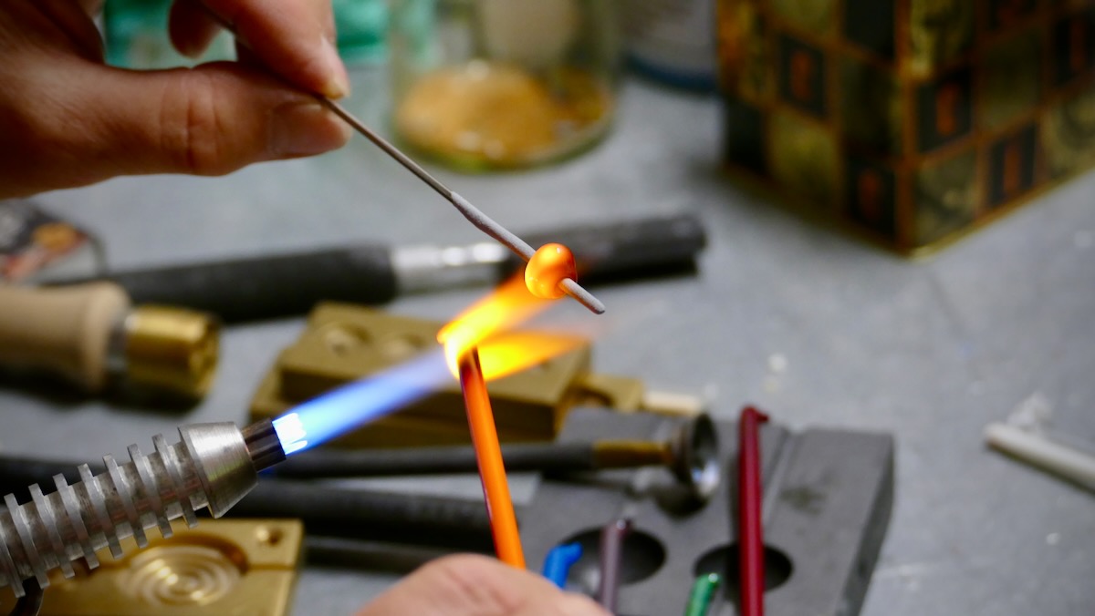 Nahaufnahme einer orangen Glasperle beim Formen über einer blauen Flamme