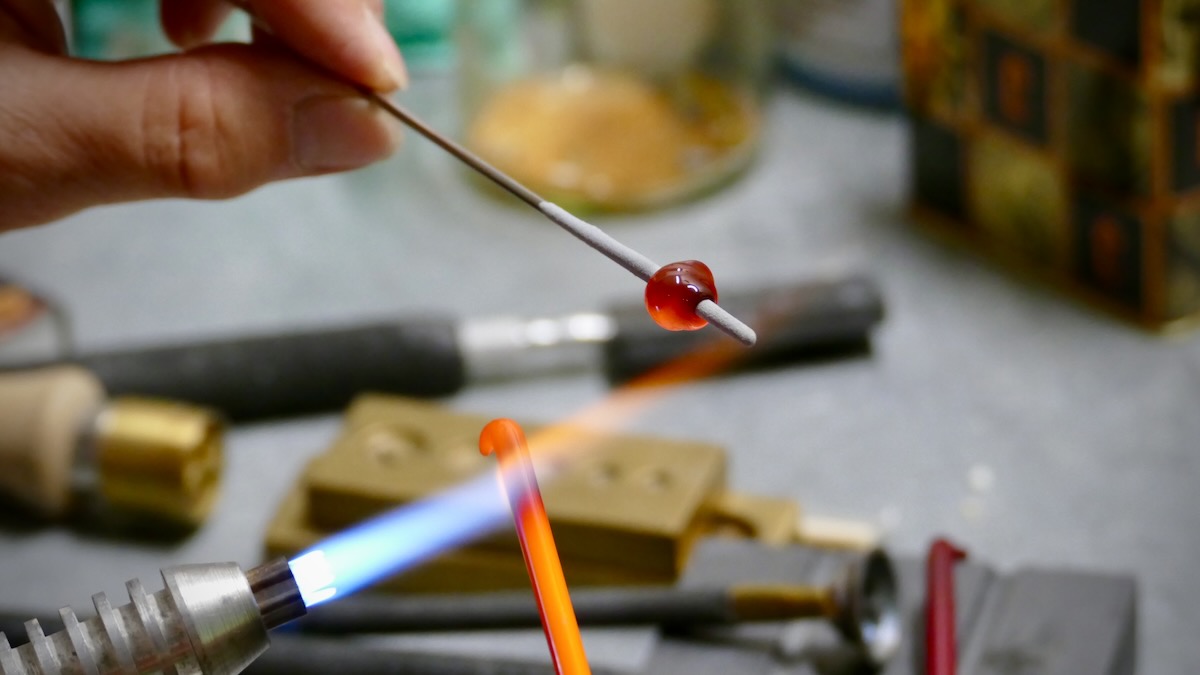 Rote Glasperle auf einem Metallstab über einer blauen Flamme