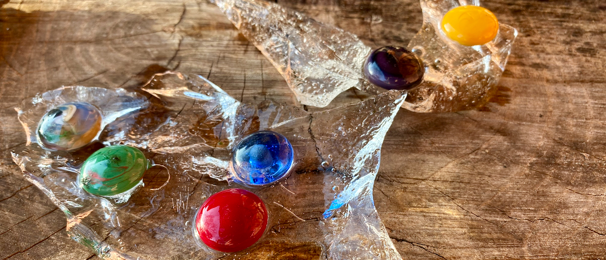 Sieben farbige Glaskugeln auf transparentem Glas und Holz